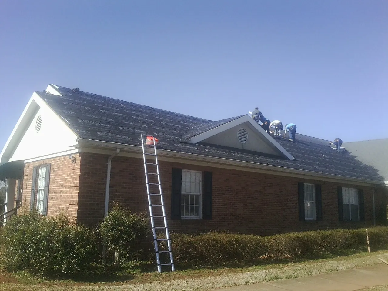 Crew tearing shingles off a brick ranch roof with a ladder set — Emergency Roof Repair work by our crew in Center Tuftonboro