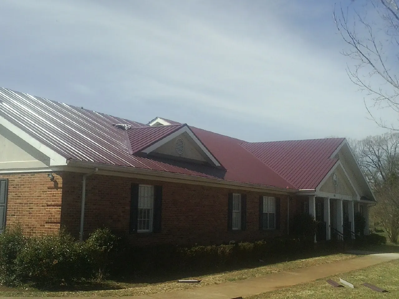 Red metal roof with gabled entries on a long brick building, from a Hail Damage Roof Repair job in Center Tuftonboro