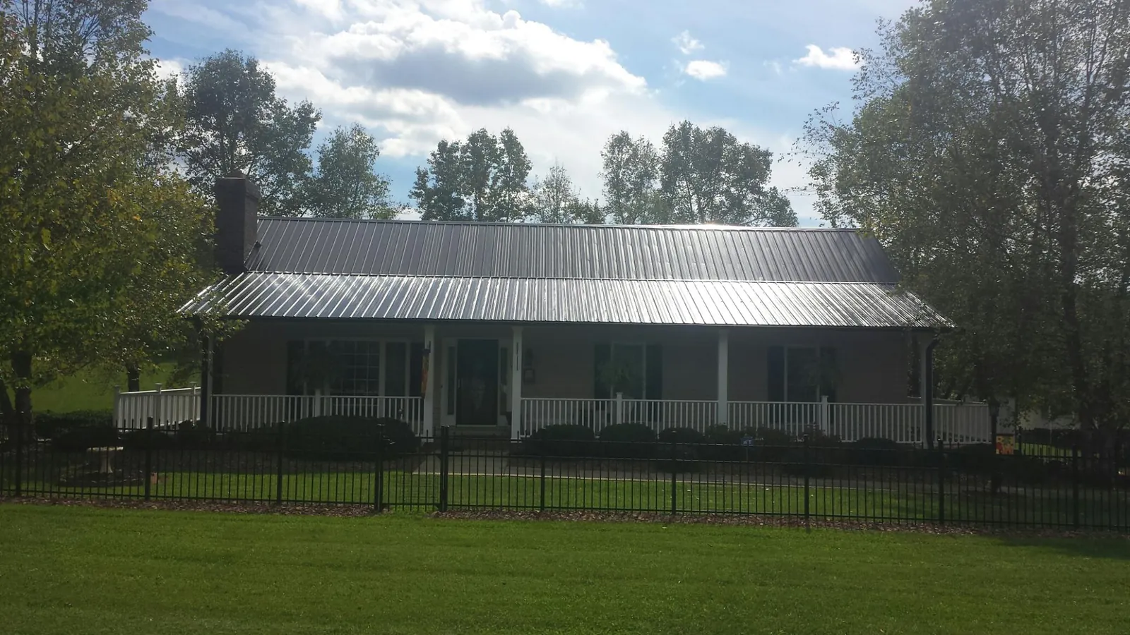 Gray metal roof on a brick ranch with a full width front porch — Gutter Guard Installation work by our crew in Center Tuftonboro