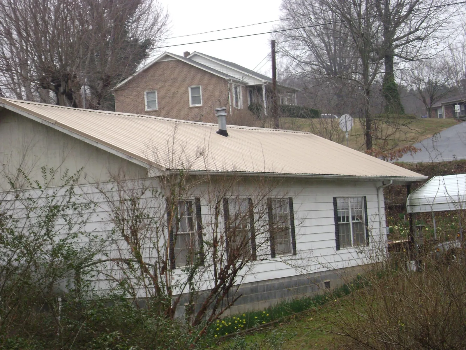 Tan metal roof on a white sided house set into a hillside — Commercial Roofing by Roofing Brothers in Center Tuftonboro