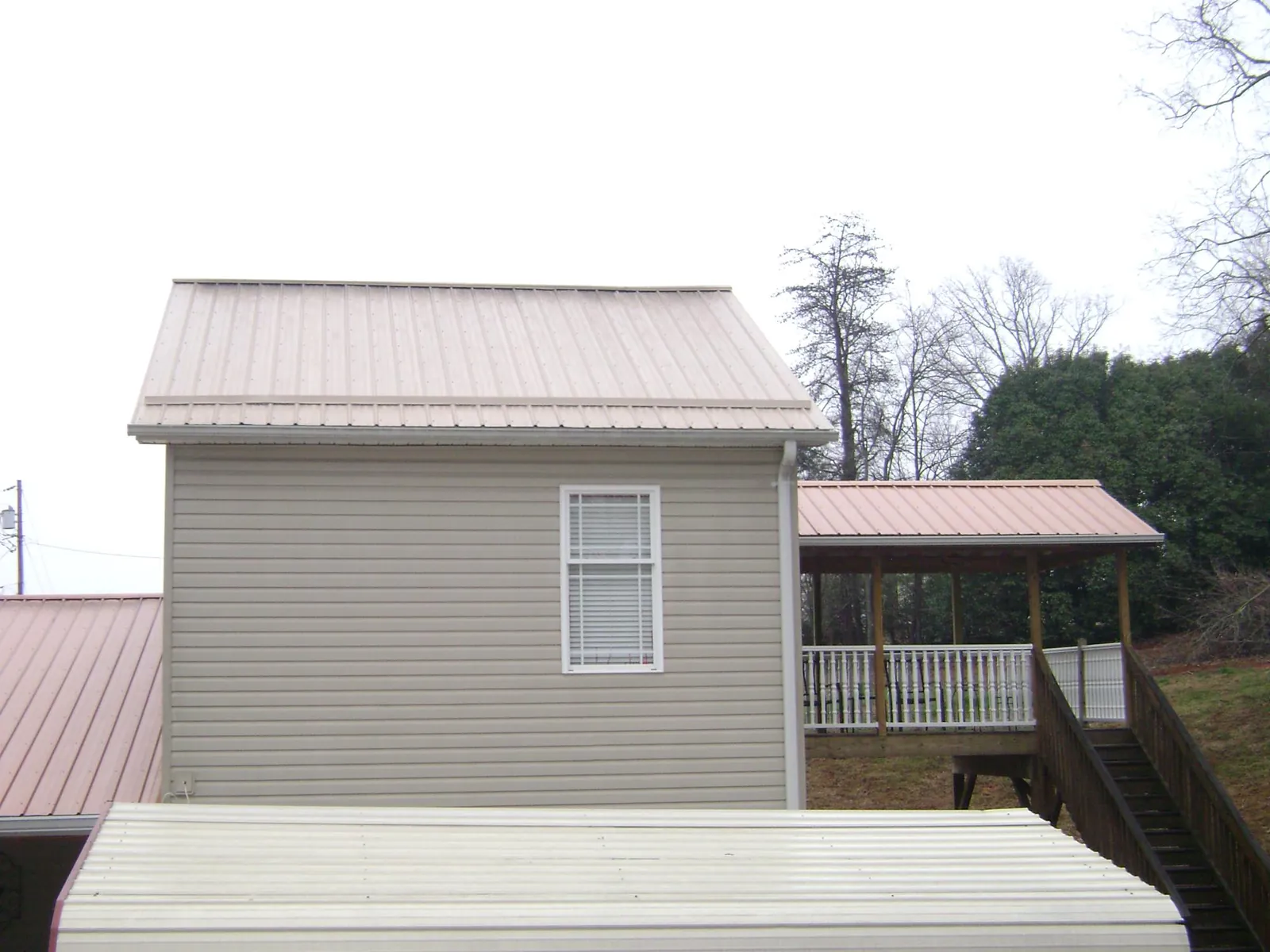 Tan metal roofs on a two story addition and attached porch, from a Roof Replacement job in Center Tuftonboro